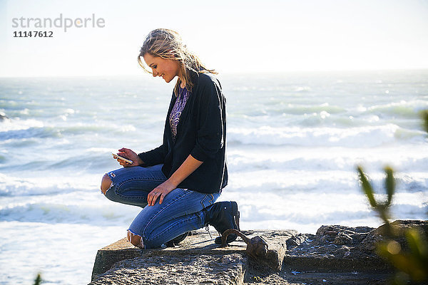 Kaukasisches Mädchen benutzt Handy auf einer Anhöhe mit Blick auf das Meer