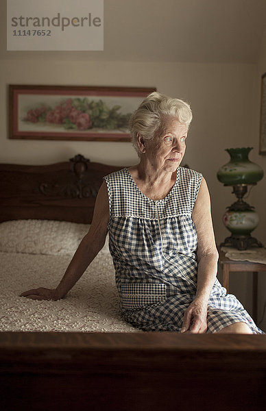 Nachdenkliche ältere Frau auf dem Bett sitzend