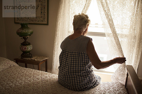 Nachdenkliche ältere Frau schaut aus dem Schlafzimmerfenster