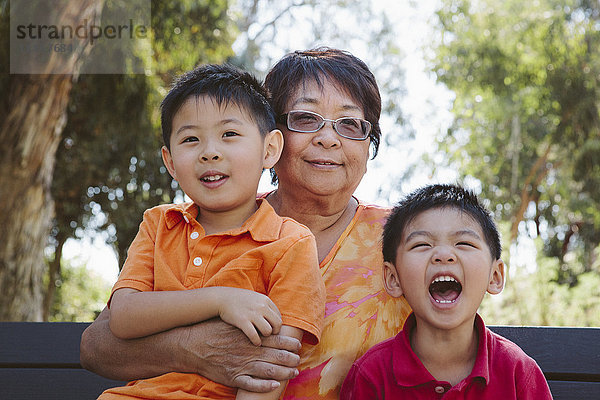 Asiatische Großmutter sitzt mit Enkelkindern auf einer Bank