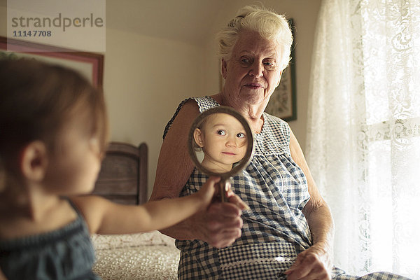 Großmutter hält Spiegel für Enkelin auf Bett