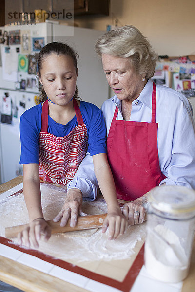 Großmutter und Enkelin rollen Teig in der Küche