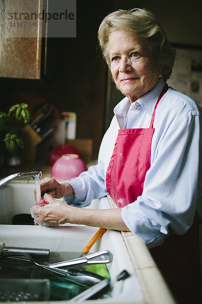 Ältere Frau wäscht Geschirr in der Spüle