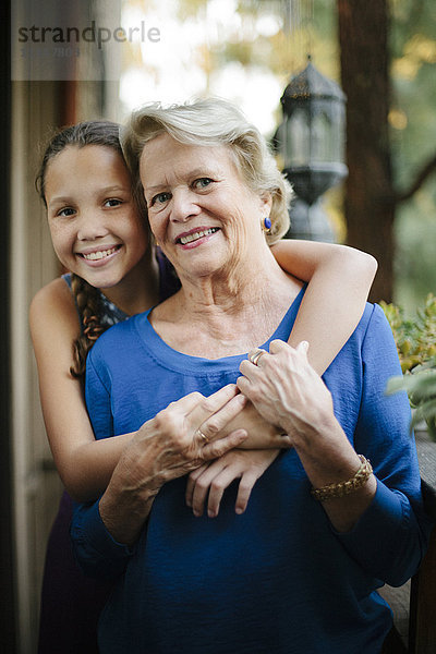 Großmutter und Enkelin umarmen sich auf der Veranda