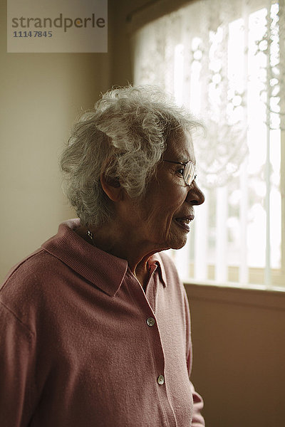 Ältere gemischtrassige Frau am Fenster stehend