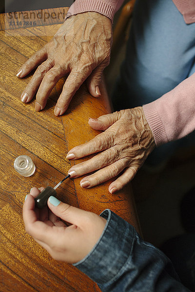 Enkelin beim Lackieren der Fingernägel der Großmutter