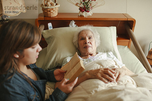 Enkelin liest Großmutter im Bett vor