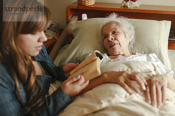 Enkelin liest Großmutter im Bett vor