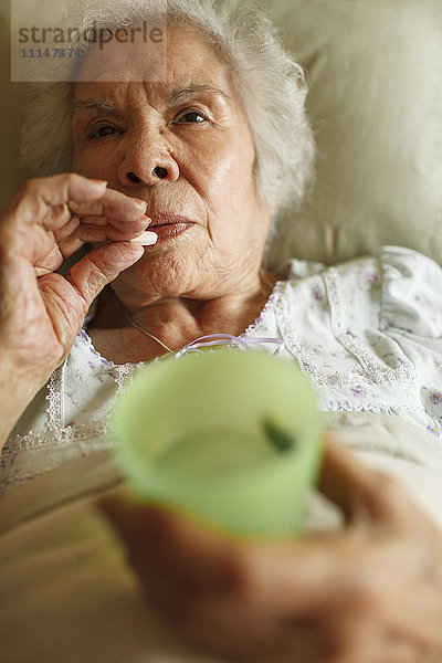Ältere gemischtrassige Frau  die im Bett Medikamente einnimmt