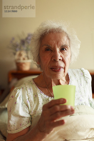 Ältere gemischtrassige Frau trinkt Wasser im Bett