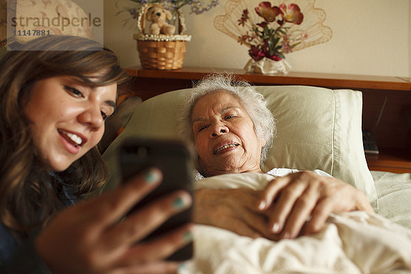 Großmutter und Enkelin machen Selfie mit Handy im Bett