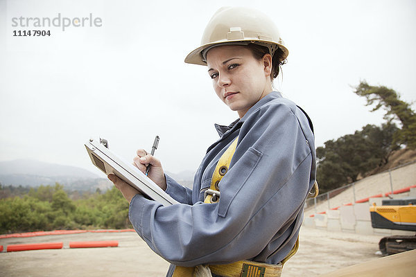 Arbeiter  der auf einer Baustelle auf einem Klemmbrett schreibt