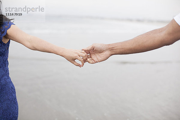 Nahaufnahme eines händchenhaltenden Paares am Strand
