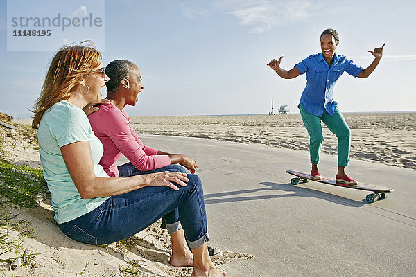 Ältere schwarze Frau  die mit Freunden am Strand Skateboard fährt