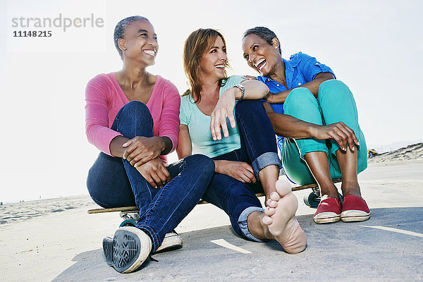 Ältere Frauen sitzen auf einem Skateboard am Strand