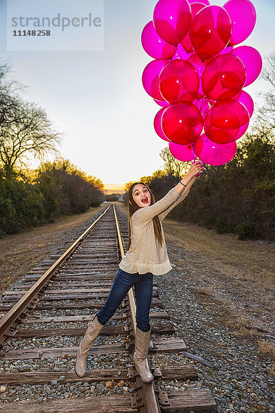 Kaukasisches Teenager-Mädchen hält ein Bündel Luftballons auf Bahngleisen