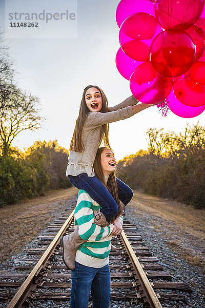 Kaukasisches Teenager-Mädchen trägt Schwester auf den Schultern mit Luftballons