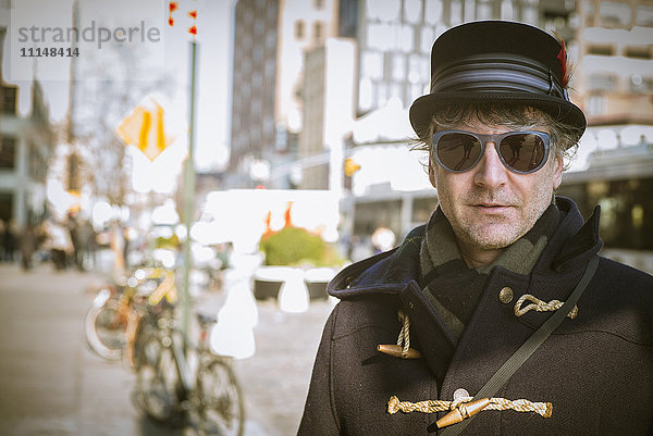 Kaukasischer Mann mit Zylinder auf dem Bürgersteig einer Stadt