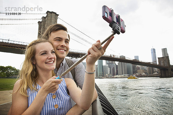Kaukasisches Paar macht Selfie mit Handy unter der Brooklyn Bridge  Brooklyn  New York  Vereinigte Staaten