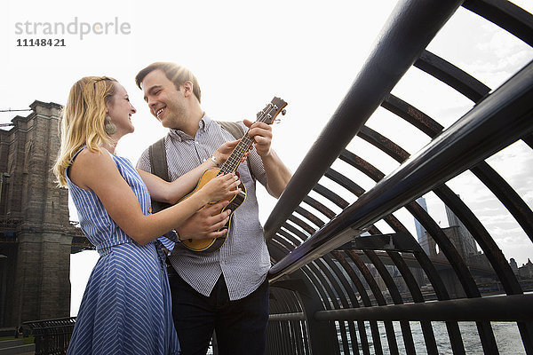 Kaukasisches Paar spielt Ukulele am städtischen Hafenviertel