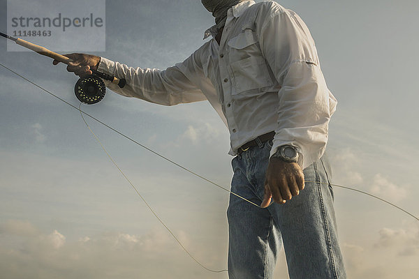 Nahaufnahme eines kaukasischen Mannes beim Fischen unter blauem Himmel
