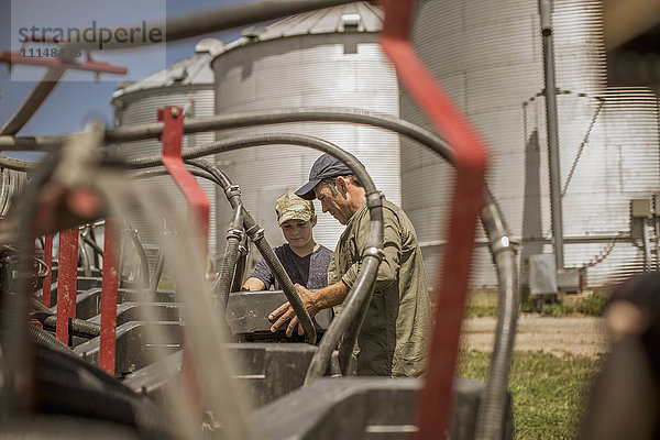 Kaukasischer Landwirt erklärt seinem Sohn auf dem Bauernhof die Maschinen