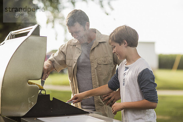 Kaukasischer Vater und Sohn grillen Essen im Garten