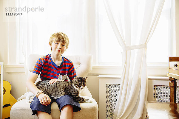 Kaukasischer Junge streichelt Katze im Wohnzimmer