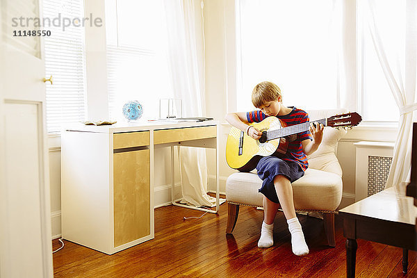 Kaukasischer Junge spielt Gitarre im Wohnzimmer