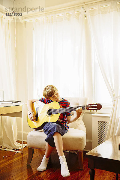 Kaukasischer Junge spielt Gitarre im Wohnzimmer