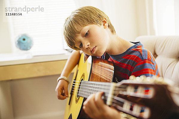 Kaukasischer Junge spielt Gitarre im Wohnzimmer