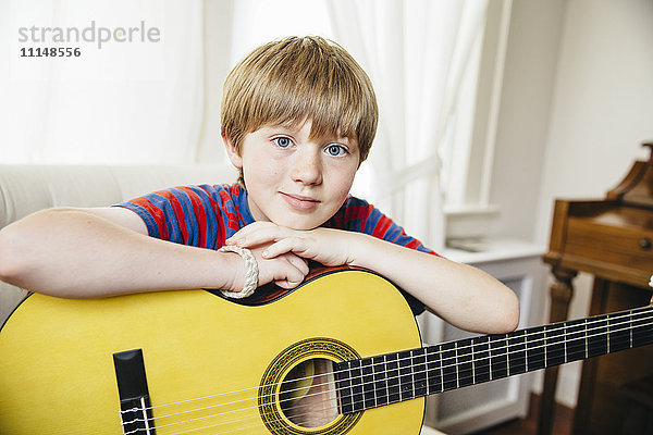 Kaukasischer Junge hält Gitarre im Wohnzimmer