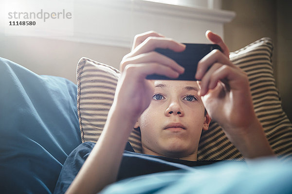 Kaukasischer Junge benutzt Mobiltelefon auf dem Bett