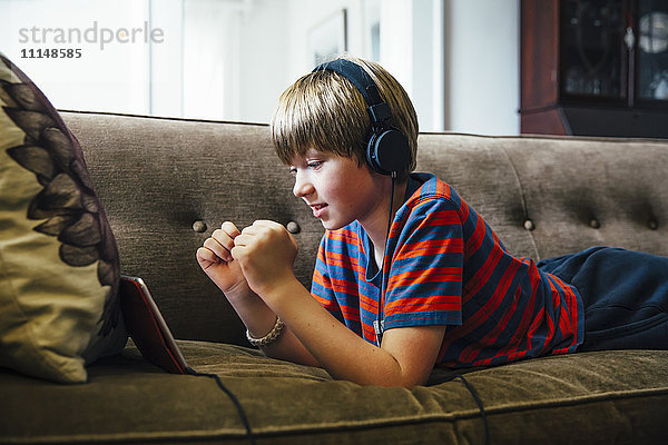 Kaukasischer Junge mit digitalem Tablet auf dem Sofa