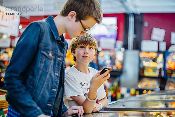 Kaukasische Brüder benutzen ein Handy in einer Spielhalle