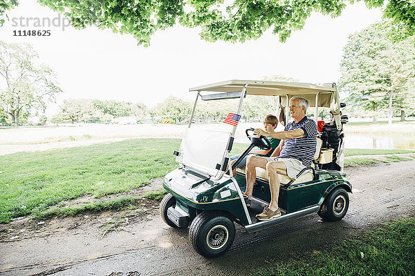 Kaukasischer Großvater und Enkel fahren Golfwagen auf dem Platz