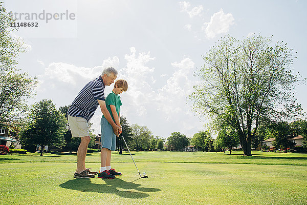 Kaukasischer Großvater bringt seinem Enkel auf dem Golfplatz Golf bei