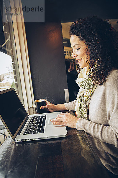 Frau benutzt Laptop und trinkt Kaffee in einem Cafe