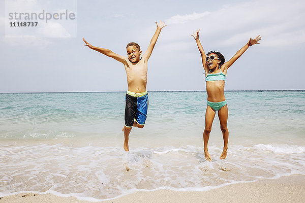 Gemischtrassige Kinder springen vor Freude am Strand