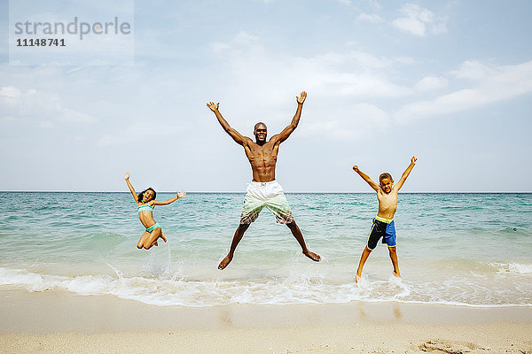 Vater und Kinder springen vor Freude am Strand