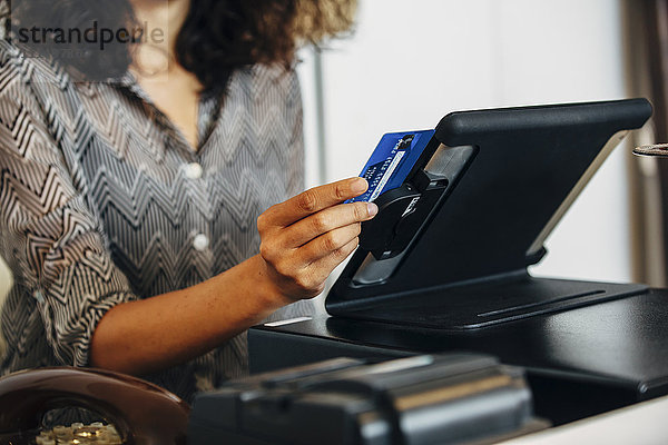Gemischtrassiger Angestellter beim Durchziehen der Kreditkarte an der Kasse
