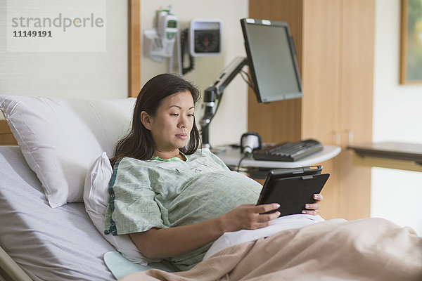 Schwangere Chinesin im Krankenhauszimmer mit digitalem Tablet