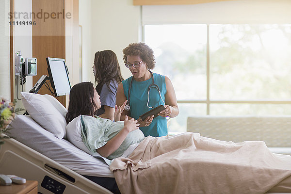 Arzt spricht mit schwangerer Patientin im Krankenhauszimmer