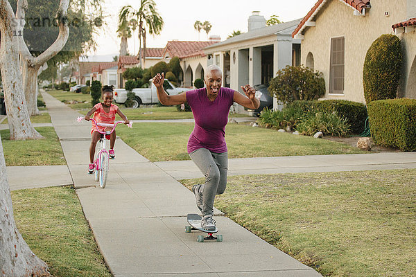 Mutter und Tochter fahren Skateboard und Fahrrad auf dem Bürgersteig
