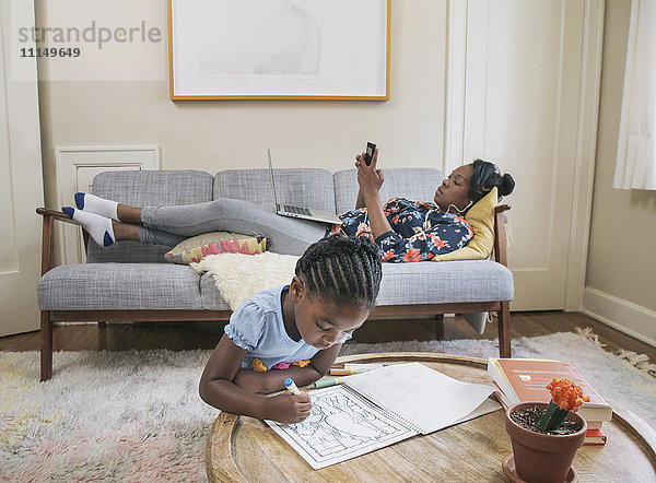Afroamerikanische Mutter und Tochter entspannen sich im Wohnzimmer