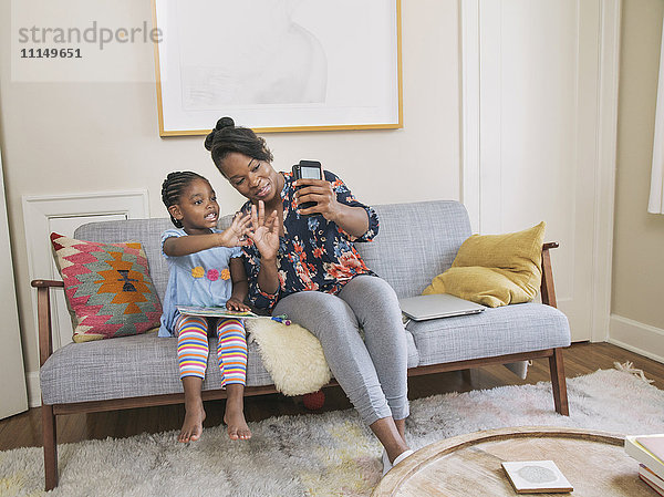 Afroamerikanische Mutter und Tochter machen ein Selfie im Wohnzimmer