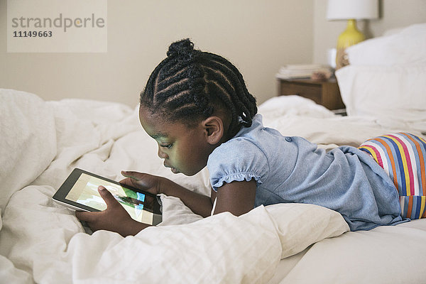 Afroamerikanisches Mädchen mit digitalem Tablet auf dem Bett