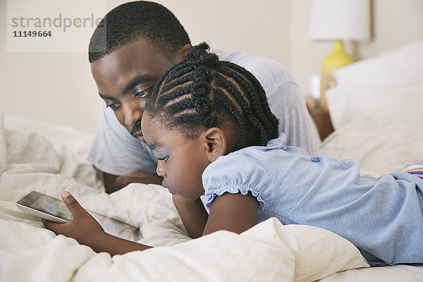 Afroamerikanischer Vater und Tochter benutzen digitales Tablet auf dem Bett