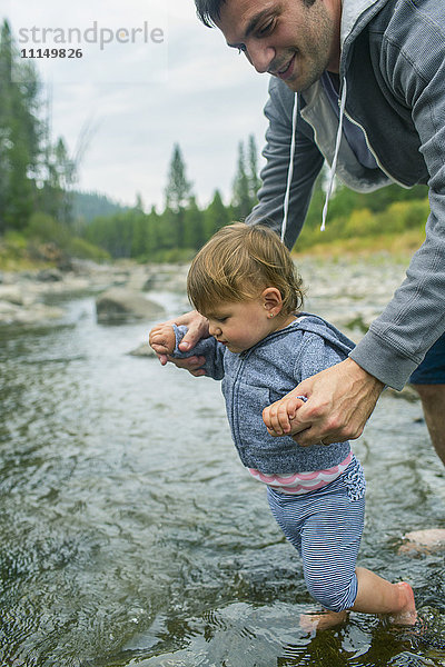 Vater hilft Tochter beim Gehen im Fluss