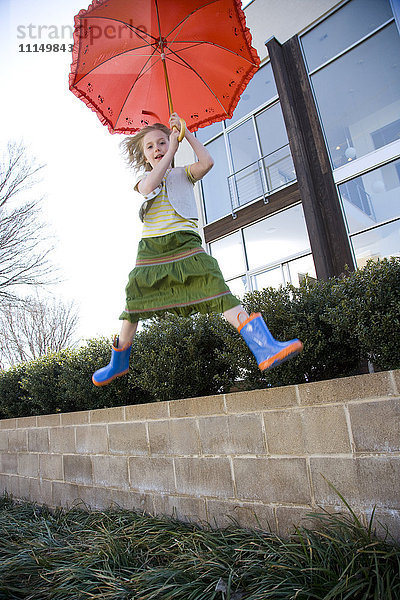 Kaukasisches Mädchen springt mit Regenschirm